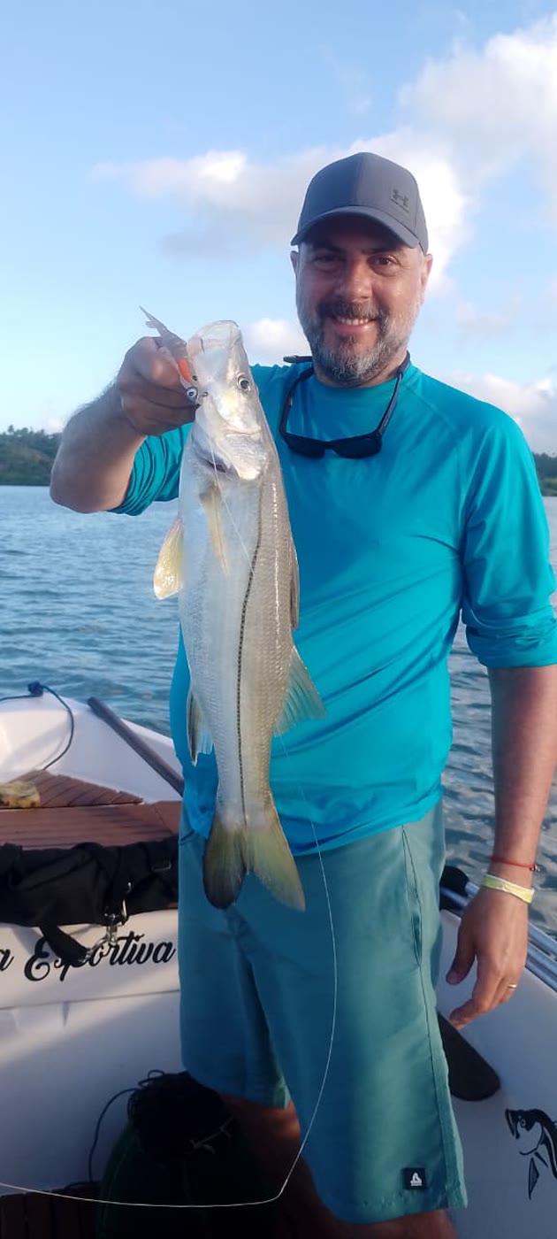 Pescador de camisa azul com um robalo e a isca na boca