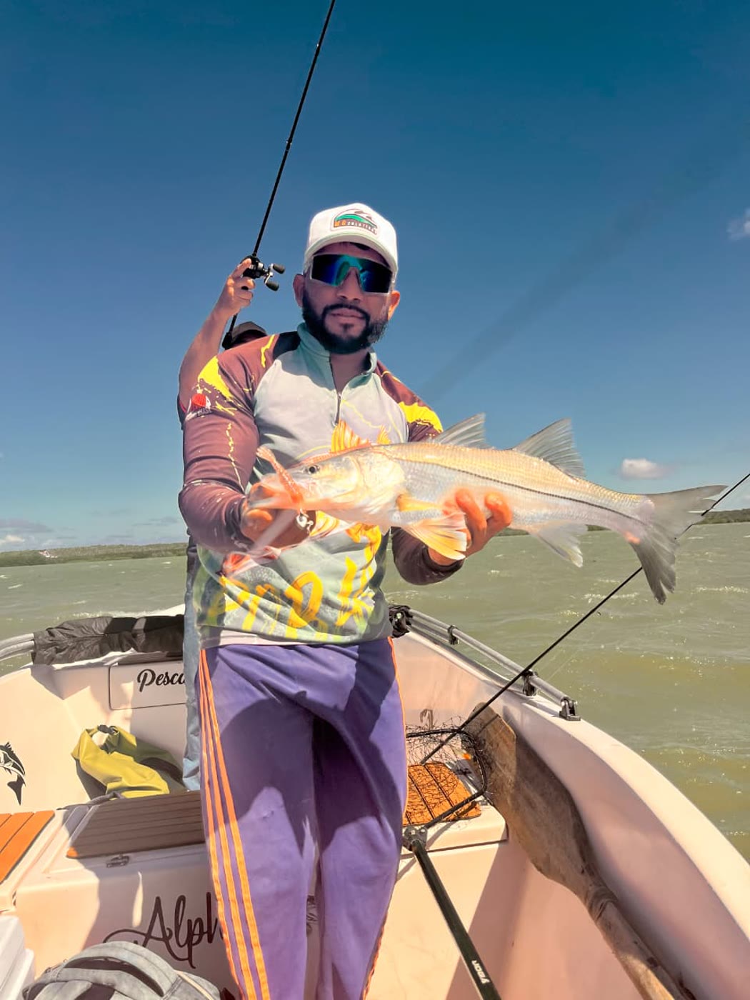 Pescador de boné branco segurando um robalo no barco