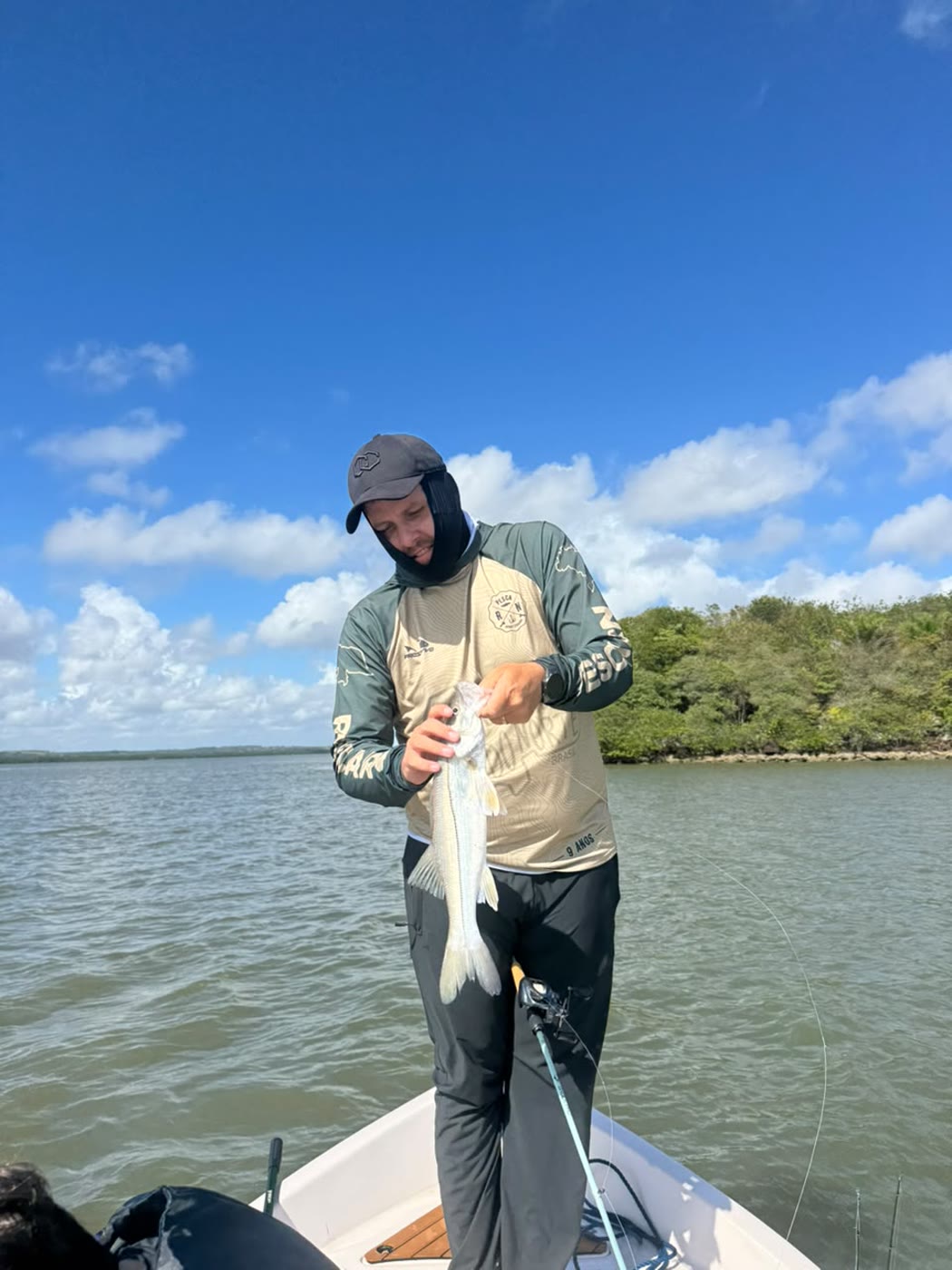 Pescador de touca com um robalo, barco na lagoa