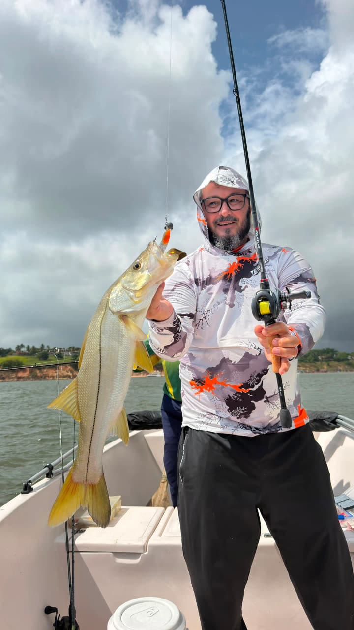 Pescador de óculos com um robalo grande, céu nublado
