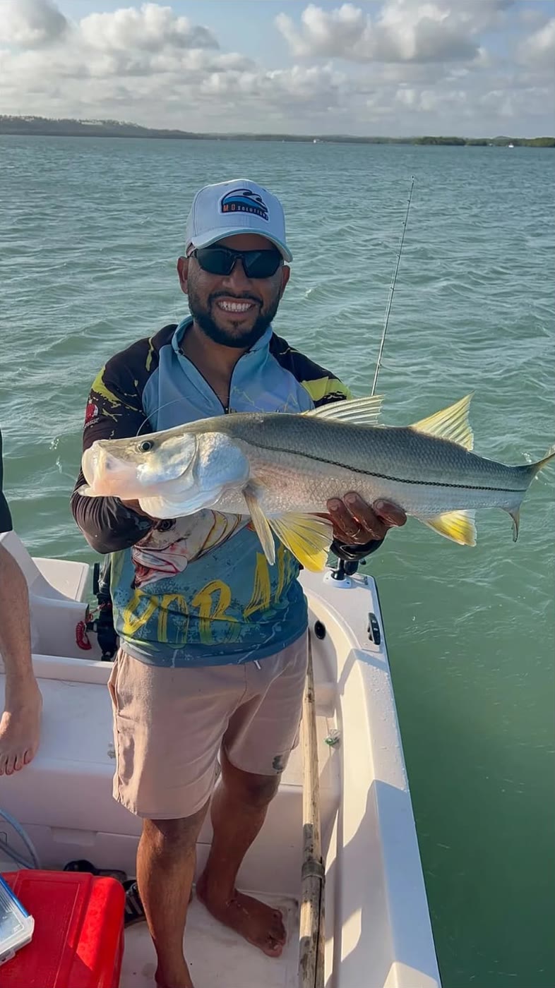 Pescador de boné branco com um robalo ao entardecer