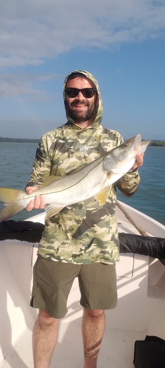 Pescador de camuflado verde com um robalo no barco
