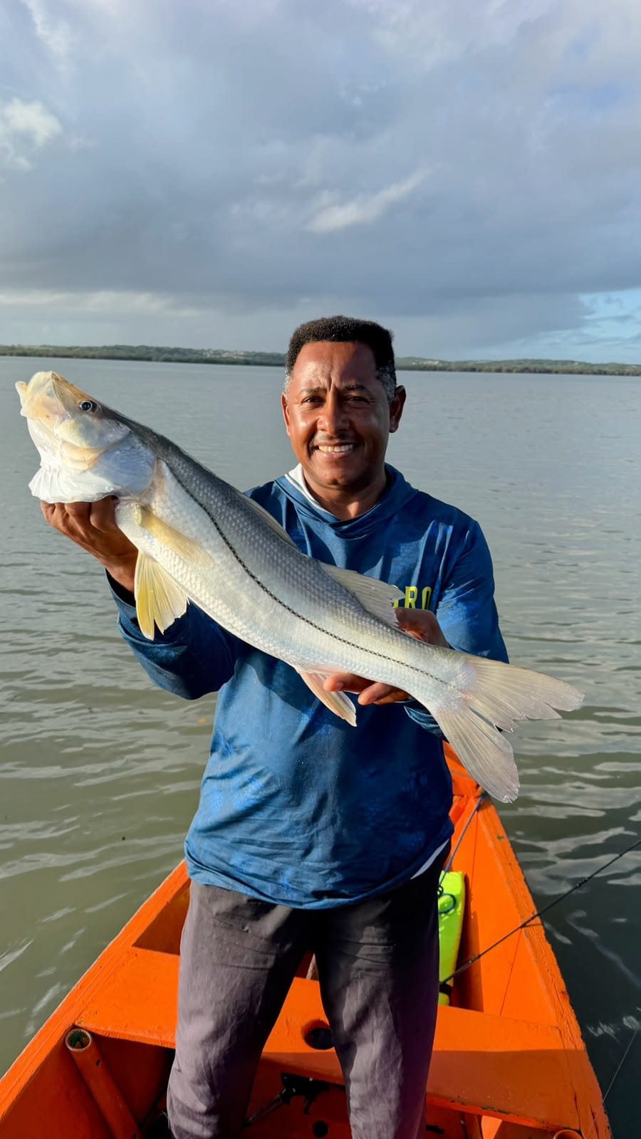 Pescador de camisa azul com um robalo grande no barco laranja